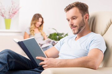 Couple at home. Cheerful young man reading book while his girlfr
