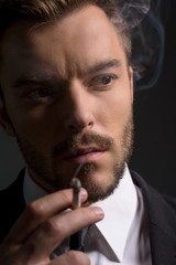 Man smoking. Bossy young man in formalwear smoking while standin