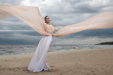 Fototapeta na wymiar model in long beige dress posing dynamic in waving fabric