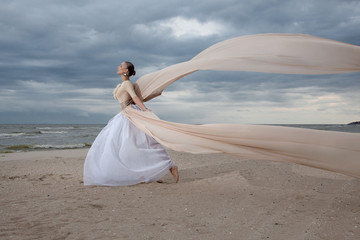 Fototapeta na wymiar model in long beige dress posing dynamic in waving fabric