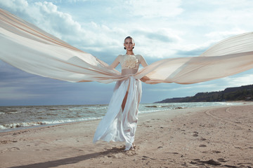 model in long beige dress posing dynamic in  waving fabric