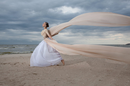 Model In Long Beige Dress Posing Dynamic In  Waving Fabric
