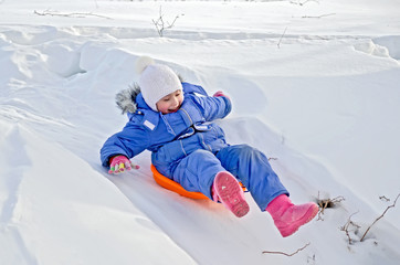 Little girl on a sled sliding on snow