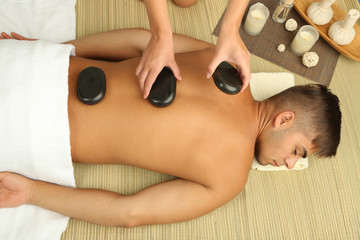 Obraz na płótnie Canvas Young man having stone massage in spa salon