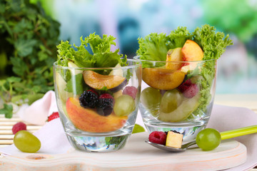 Fruit salad in glasses, on wooden table, on bright background