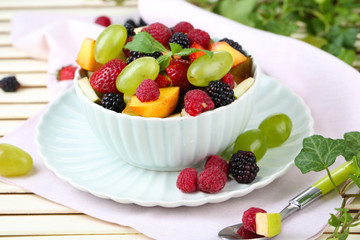 Fruit salad in bowl, on wooden table, on bright background