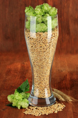 Glass of fresh green hops and barley, on wooden background