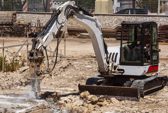 Excavator with hammer engaged in excavation of foundation