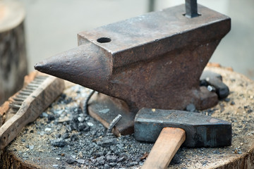 Rustic anvil and hammer on a wooden log, horizontal shot
