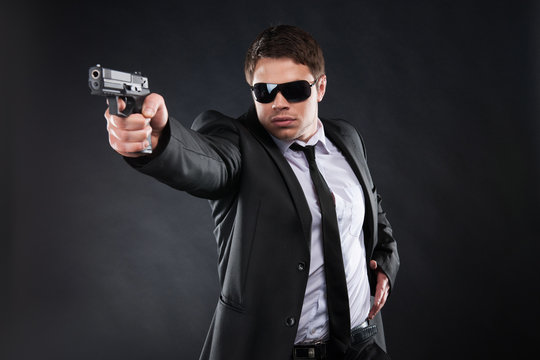 Bodyguard. Confident young man in formalwear holding gun and aim