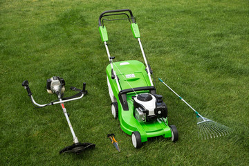 Green lawnmower, weed trimmer, rake and secateurs on the lawn
