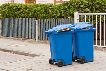 Blaue M&uuml;lltonnen f&uuml;r Altpapier stehen am Strassenrand