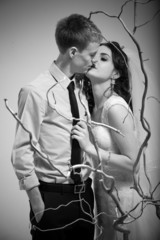 Black and white portrait of married couple kissing behind tree