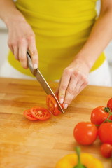 Closeup on young housewife cutting tomato on cutting board
