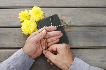 Hands with rosary over old Holy Bible. Wooden background.