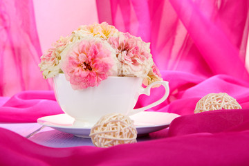 Roses in cup on wooden table on pink cloth background