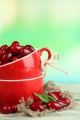 Fresh cornel berries in red cups on wooden table