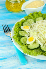 Delicious salad with eggs, cabbage and cucumbers on blue table