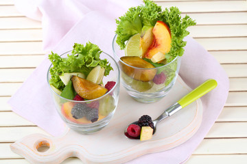 Fruit salad in glasses, on wooden background