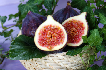 Ripe figs in basket in leaves on wooden table close-up