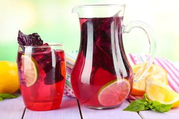 Red basil lemonade in jug and glass, on  bright background