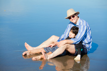 Father playing with disabled son on beach, holding him upright