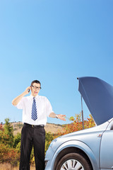 Young man standing near a broken car and talking on a phone