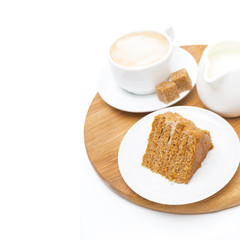 piece of honey cake, jug of cream and cup of cappuccino on board