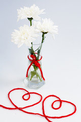 White flowers in a small glass vase and two hearts from threads