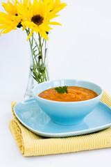 Pumpkin soup in a blue plate and a bouquet of yellow flowers