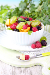 Fruit salad in bowl, on wooden table, on bright background