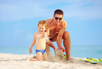 happy father and son having fun in sand on the beach