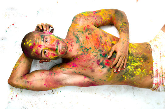 Young man shirtless laying on floor, skin painted with colors