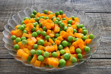 Boiled carrots with green peas in glass bowl