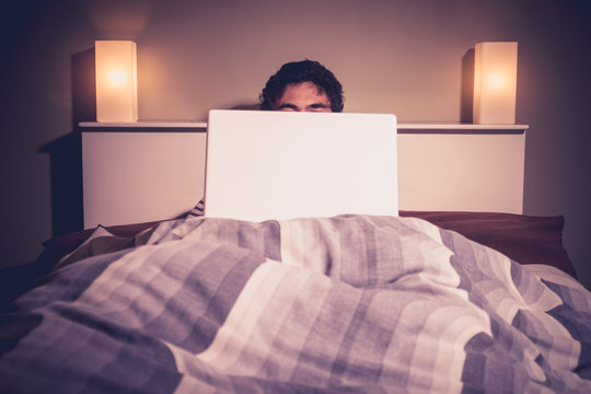 Man is sitting in bed behind his laptop