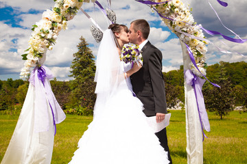 First kiss of newly married couple under wedding arch
