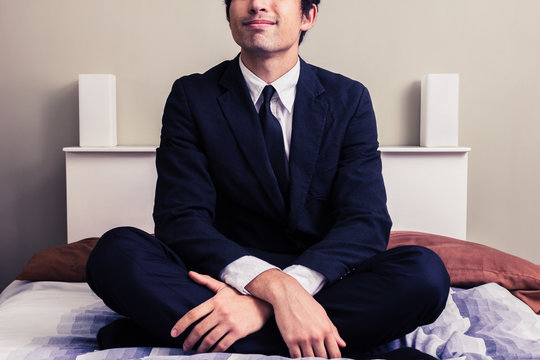 Happy young businessman sitting on bed