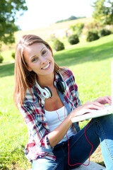 Cheerful girl sitting against tree with laptop