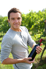 Young winegrower presenting wine bottles