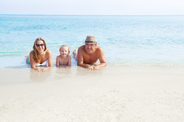Fototapeta premium Happy family laying on the sand enjoying the ocean