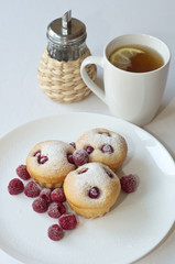 Cupcakes with raspberries on white plate with cup of tea
