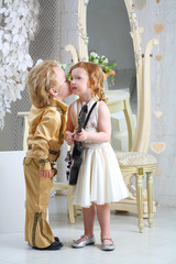 Little boy in pop retro suit kisses a girl in white dress