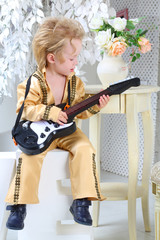 Portrait of a little boy in pop retro suit playing the guitar