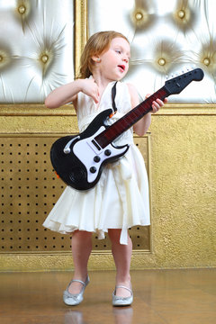 A small girl in white dress sings and plays guitar