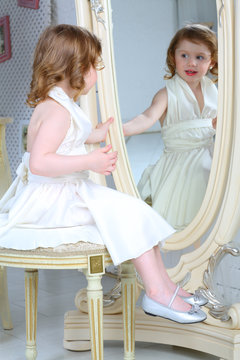 A little girl dressed admires her reflection in mirror