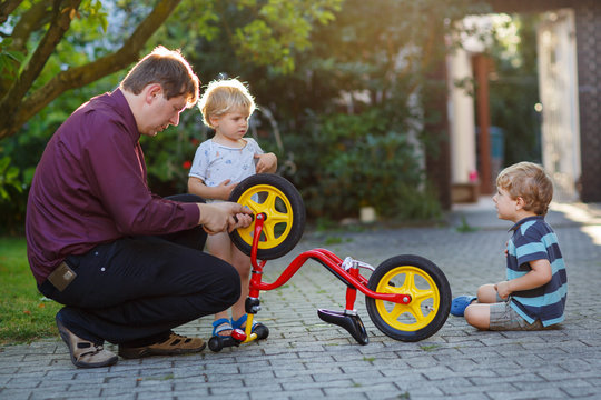 Portrait of two cute boys repairing bicycle wheel with father ou