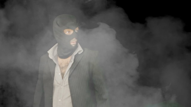 Masked criminal into smoke looking around