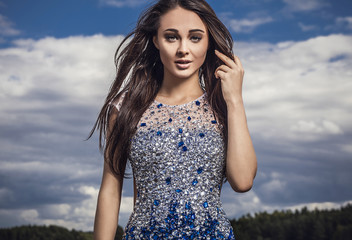 Young woman in fashionable dress pose outdoor on sky background.