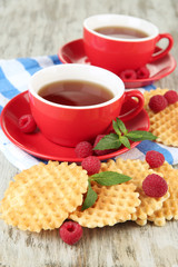 Cups of tea with cookies and raspberries on table close-up