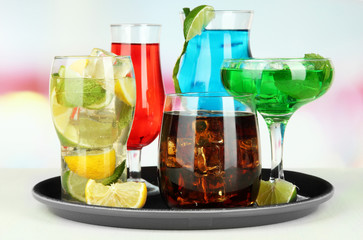Many glasses of cocktails on tray on table, on bright